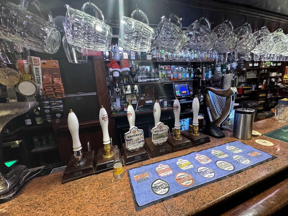 The bar top with a row of white ceramic hand pumps and cask ale clips, glasses hanging upside down above, and bottles on the back shelves.